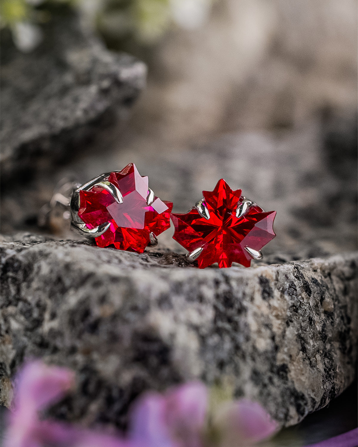 Sterling silver maple leaf ruby stud earrings displayed on natural granite stone.