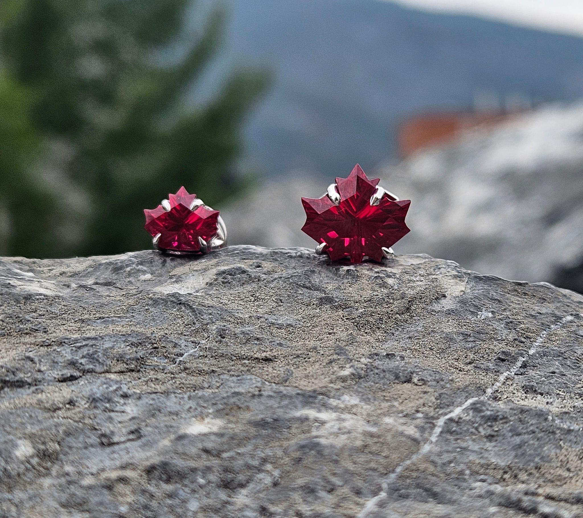 Red maple leaf earrings on a rock with a blurred natural background